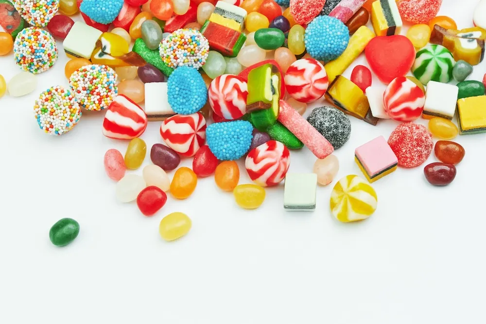 Bunte Mischung aus Süßigkeiten, darunter Gummibärchen, Bonbons, Geleebonbons, Lakritz und Schaumzucker, auf weißem Hintergrund verstreut.