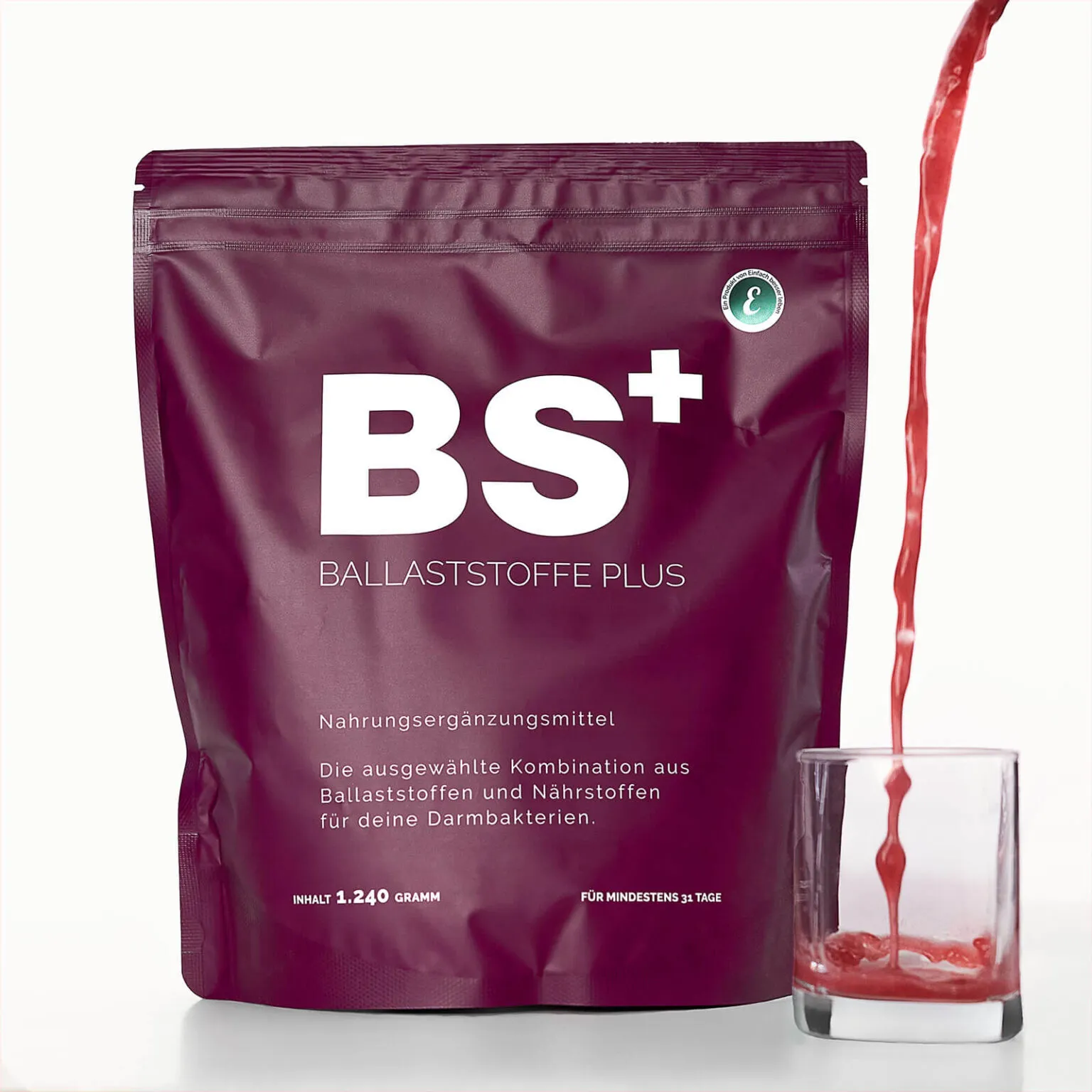 Produktverpackung von BS+ Ballaststoffe Plus mit einem roten Getränk, das daneben in ein Glas gegossen wird