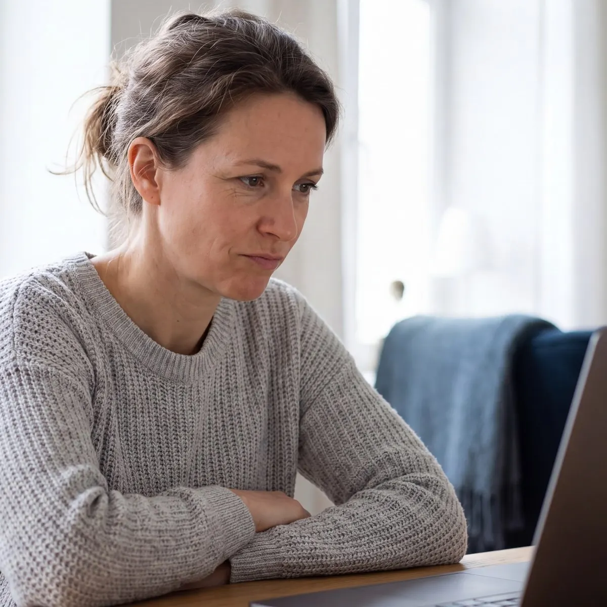 Frau sitzt nachdenklich am Tisch vor ihrem Laptop